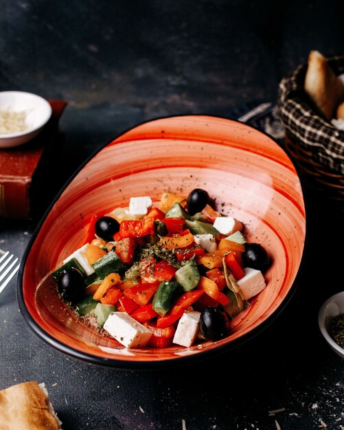 Вид спереди греческий салат с оливками помидоры белый сыр и огурцы внутри черной тарелке на темном полу