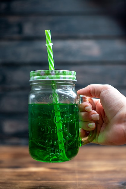 Вид спереди зеленого яблочного сока внутри банки с соломинкой на деревянном столе фото напитка коктейль-бар фруктовый цвет