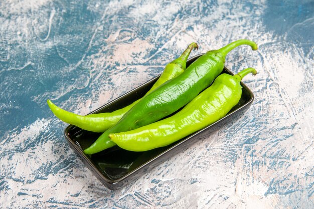 Front view green hot peppers on black plate on blue-white background with free space