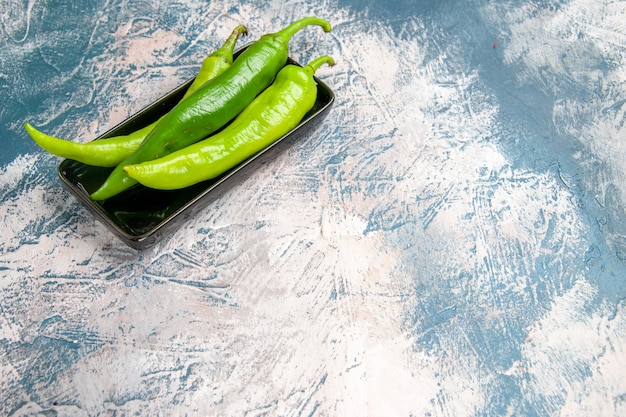 Front view green hot peppers on black plate on blue-white