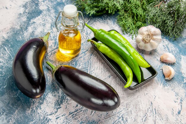 Front view green hot peppers on black plate eggplants garlic oil peppers on blue-white background