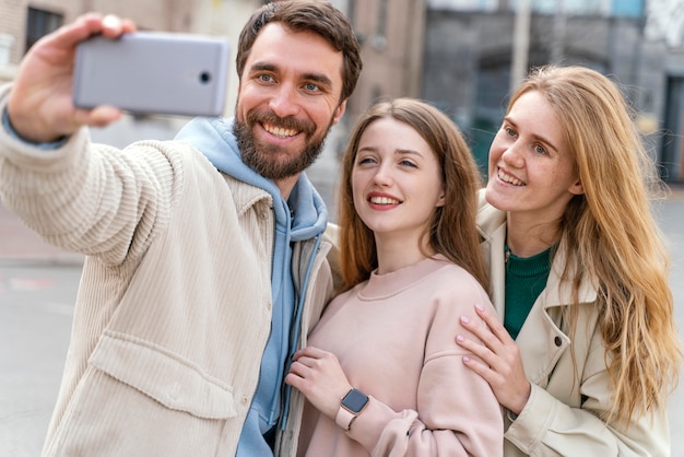 Front view of group of smiley friends outdoors in the city taking selfie
