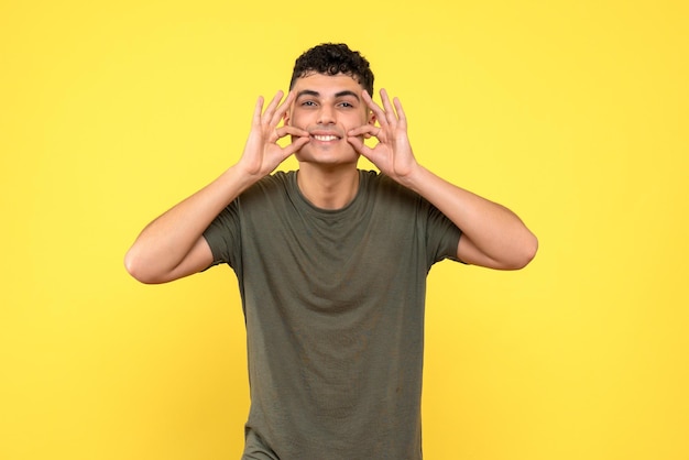 Front view of the guy with closed eyes s smiling and holds fingers near mouth