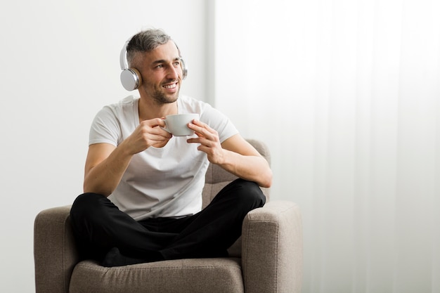 一杯のコーヒーを保持しているヘッドフォンで正面男