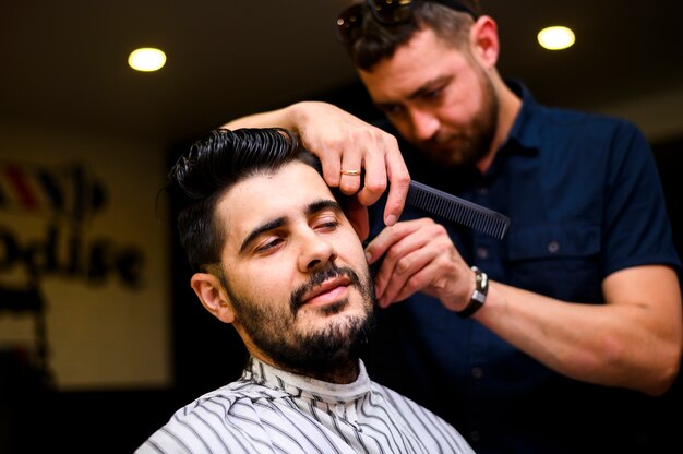 Вид спереди парикмахера-стилиста стрижет волосы клиента