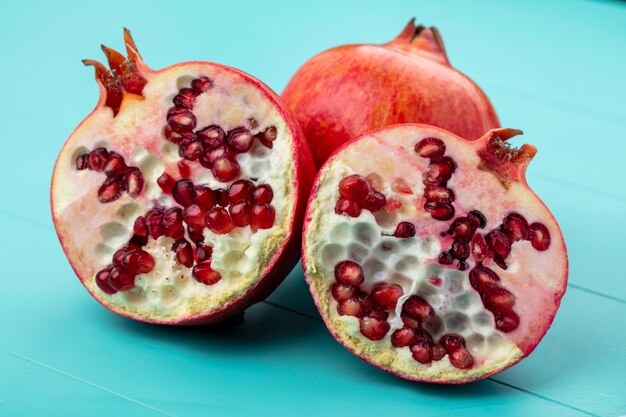 Front view of half cut pomegranate with whole one on blue surface