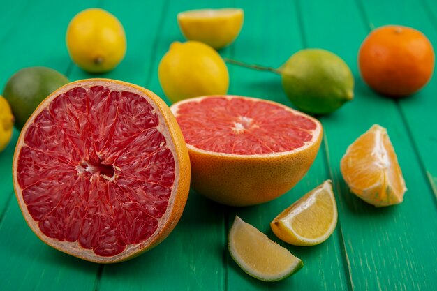 Front view halved grapefruit with peeled oranges and slices of lemon  lime on a green background