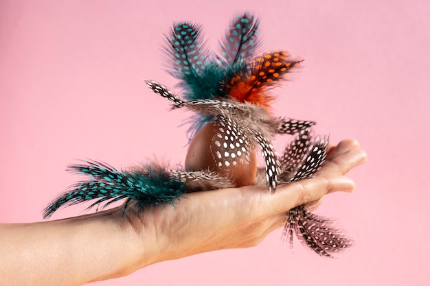 Front view of hand holding colorful painted easter eggs with feathers