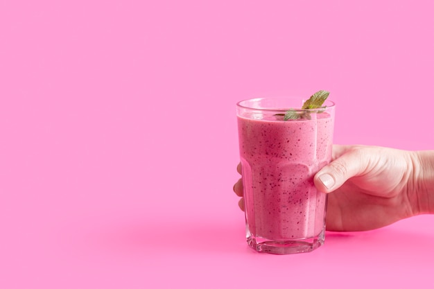 Front view hand holding glass wih pink smoothie and mint with copy-space