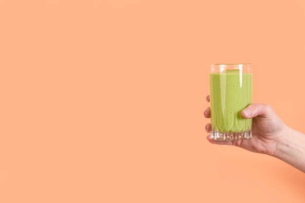 Front view hand holding green smoothie in glass with copy-space