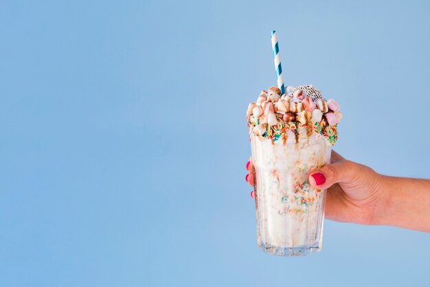 Front view of hand holding milkshake with blue background