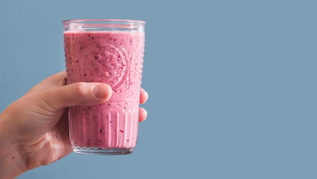 Front view hand holding pink smoothie in glass with copy-space