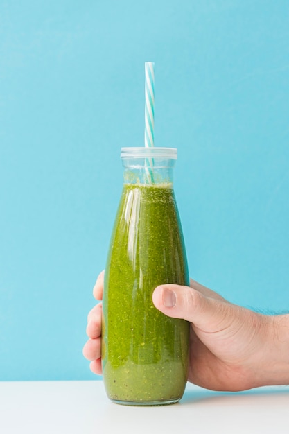 Free photo front view hand holding smoothie bottle with straw