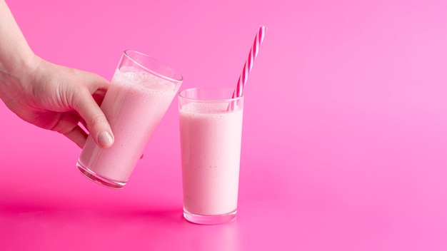 Front view hand holding smoothie glass near glass with straw