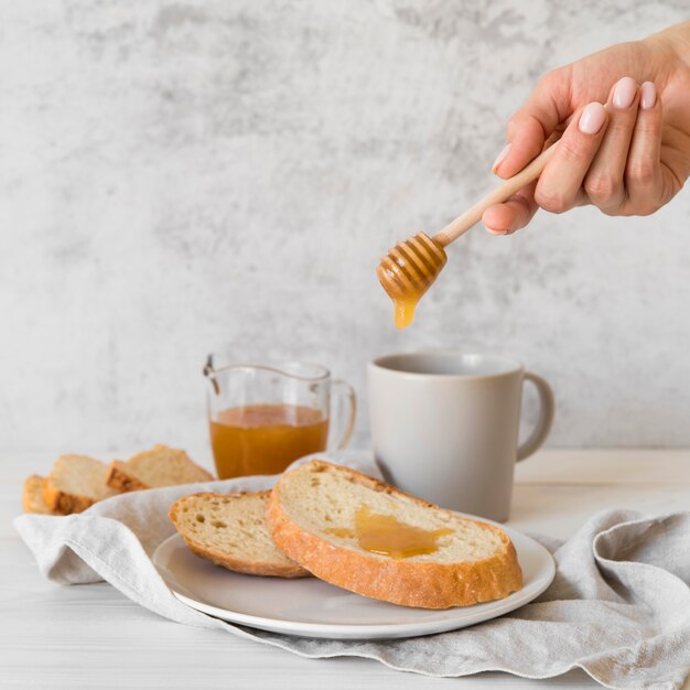 Front view hand pouring honey over slice of bread