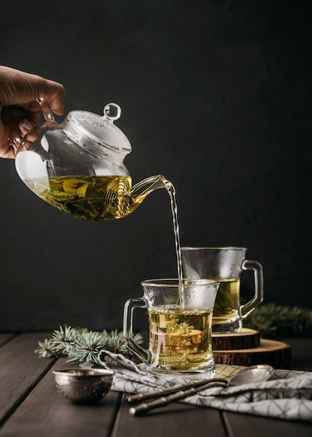 Front view hand pouring tea in glass with teapot