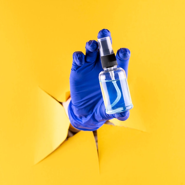 Front view of hand with surgical glove holding hand sanitizer bottle