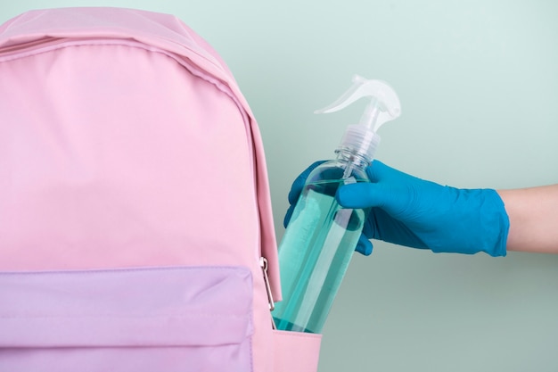 Front view of hand with surgical glove putting disinfectant bottle in book bag