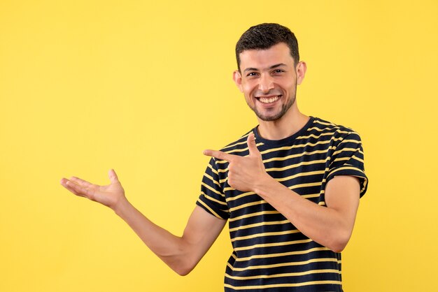 Front view handsome male in black and white striped t-shirt pointing at left on yellow isolated background