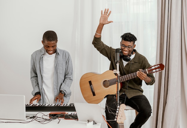 Front view of handsome male musicians at home playing electric keyboard and guitar