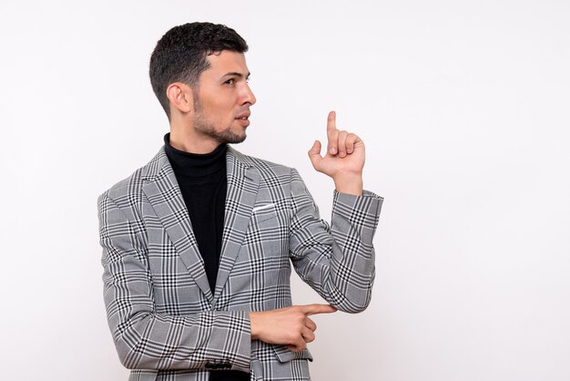 Front view handsome male in suit pointing at behind standing on white isolated background