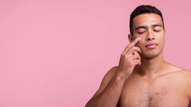 Front view of handsome man applying face cream with copy space