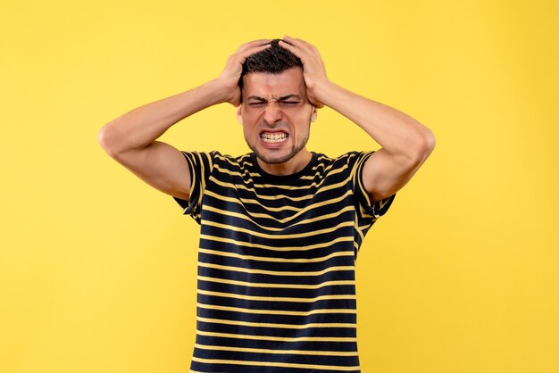 Front view handsome man in black and white striped t-shirt holding head on yellow isolated background