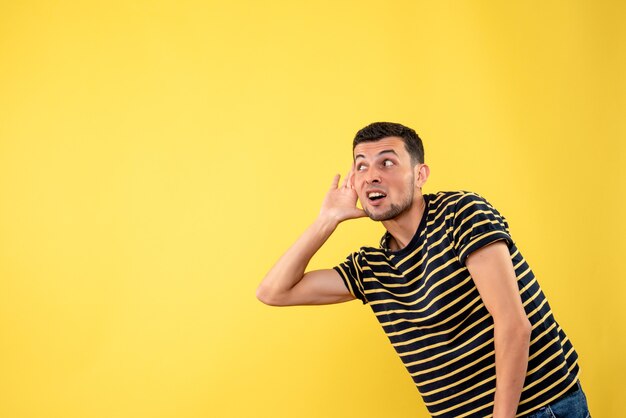 Front view handsome man in black and white striped t-shirt listening at something on yellow isolated background