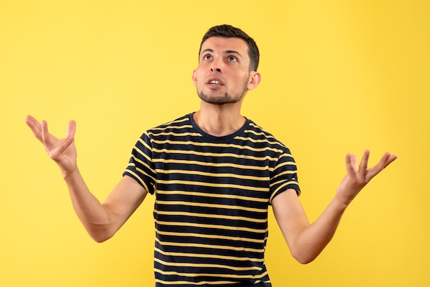 Front view handsome man in black and white striped t-shirt looking at ceiling on yellow isolated background