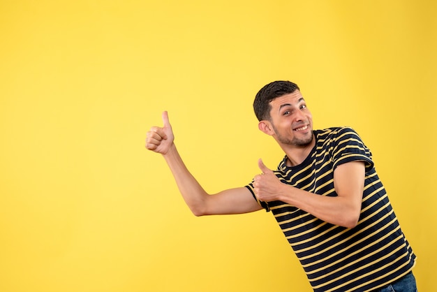Вид спереди красивый мужчина в черно-белой полосатой футболке, делая большой палец вверх знак на желтом изолированном фоне