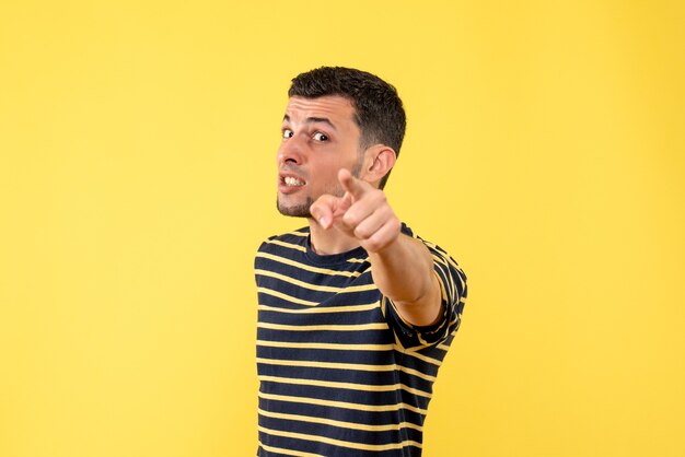 Front view handsome man in black and white striped t-shirt pointing at camera on yellow isolated background