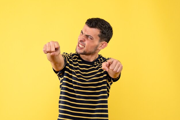 Front view handsome man in black and white striped t-shirt showing winning gesture on yellow isolated background