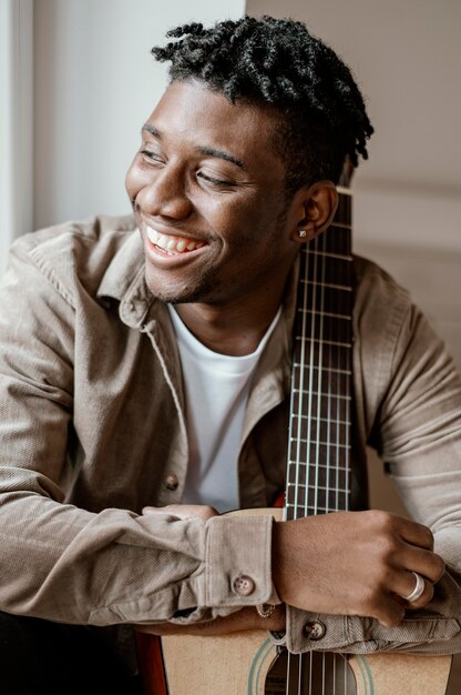 Front view of handsome smiley male musician at home posing with guitar