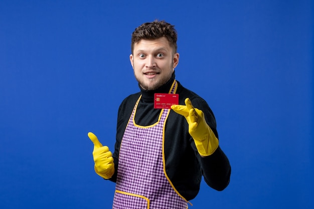 Front view handsome young man holding card making thumb up sign on blue space