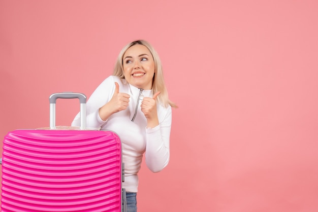 親指をあきらめるピンクのスーツケースと正面図幸せなブロンドの女性