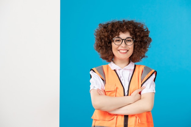 Front view of happy female builder in uniform on blue wall