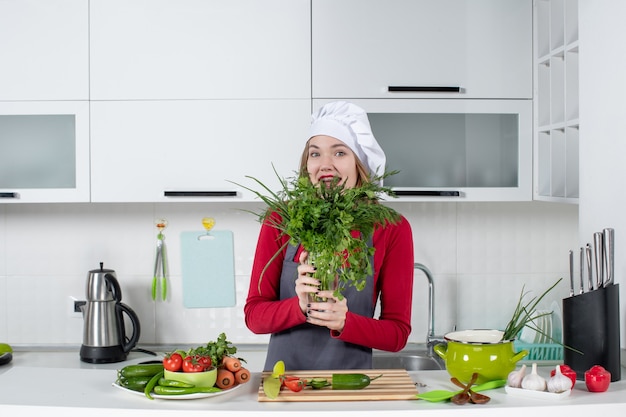 Front view happy female chef in cook hat holding up greens