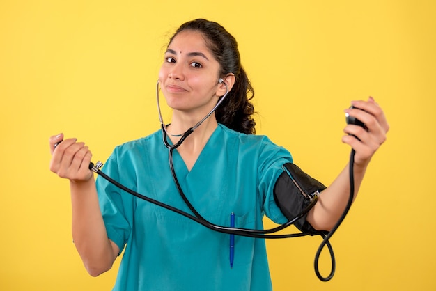 Free photo front view happy female doctor in uniform holding sphygmomanometers standing on yellow background