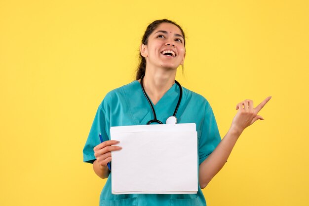 Front view happy female doctor with documents standing on yellow background