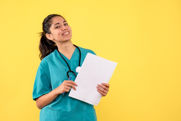 Вид спереди счастливая женщина-врач с документами на желтом фоне
