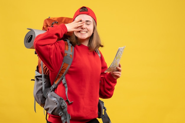 Front view happy female hiker with red backpack holding map putting hand on her eye