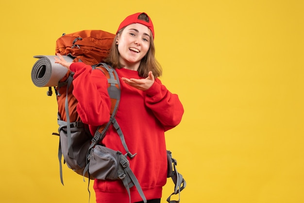 Front view happy female traveler with red cap pointing at her backpack