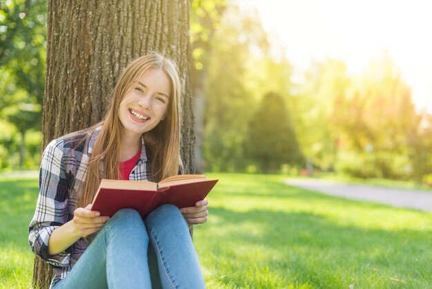 Front view happy girl reading a book while sitting on grass
