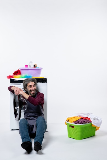 Front view happy housekeeper man sitting near laundry basket on white background