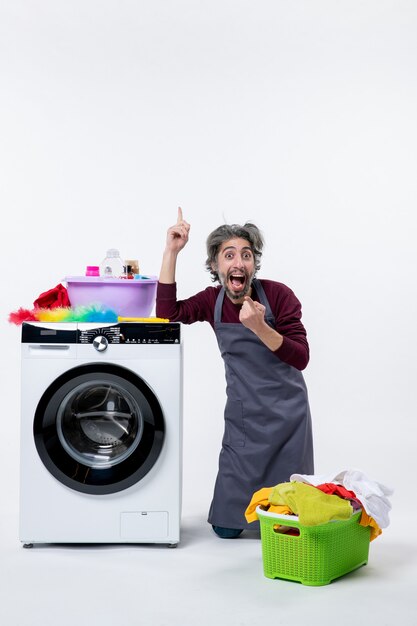 Front view happy housekeeper man standing on knee pointing with finger up on white background