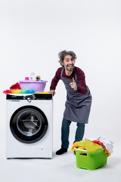 Front view happy housekeeper man standing near white washer laundry basket on floor