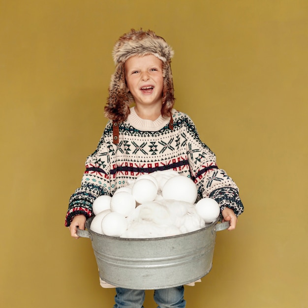 Front view happy kid with hat and snowballs