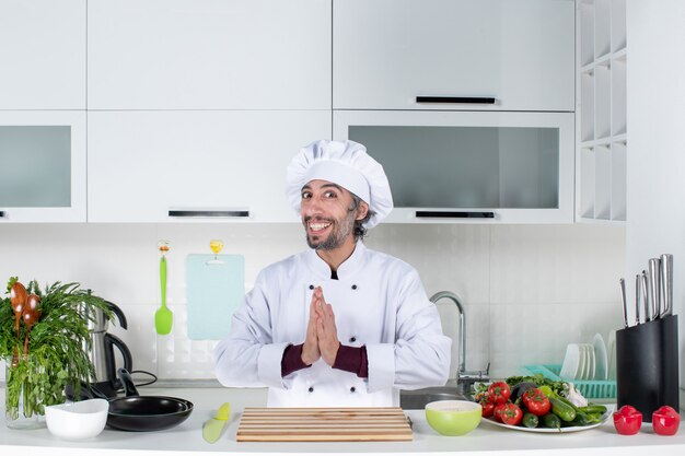 正面図キッチンテーブルの後ろに立って手をつなぐクック帽子の幸せな男性シェフ