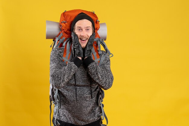 Front view of happy male hitchhiker with leather gloves and backpack putting hands on his face