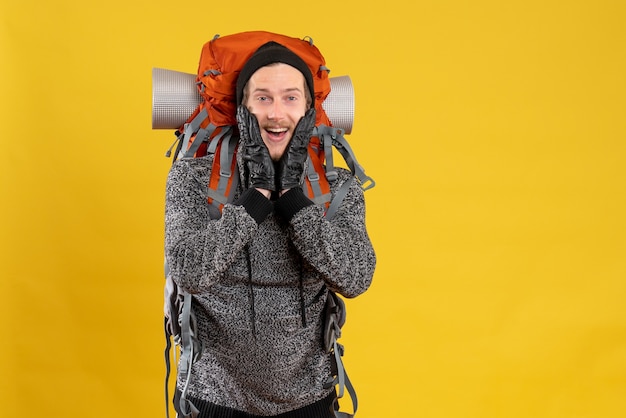 Front view of happy male hitchhiker with leather gloves and backpack putting hands on his face